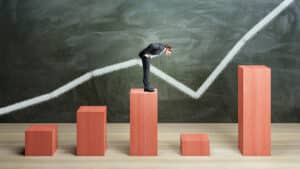 Businessman on red chart bars on chalkboard wall background crisis business and growth