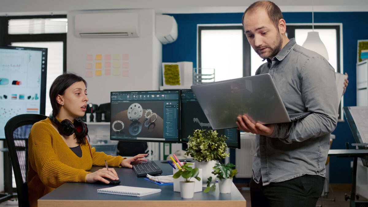 Project supervisor holding laptop and talking with engineer compering d industrial metallic pieces