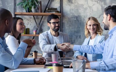 Young modern colleagues in smart casual wear shaking hands and smiling while sitting in the creative office