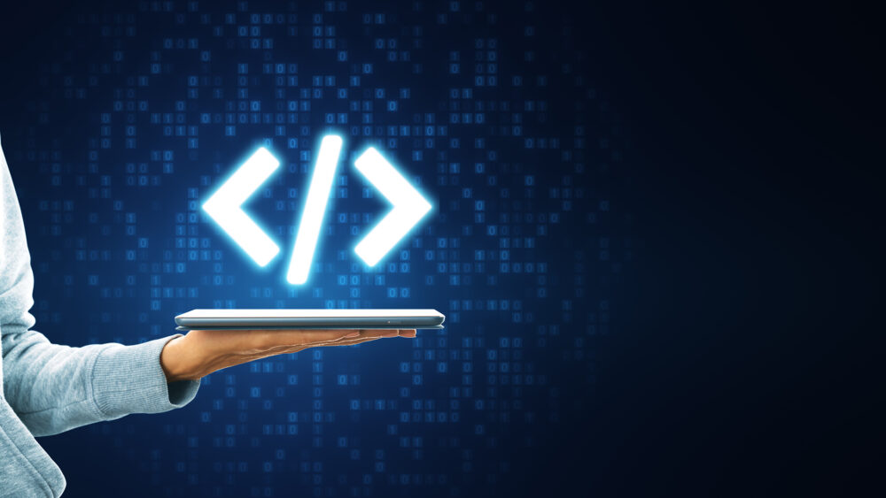Bright coding symbol on a tablet screen held by a person in a dark background