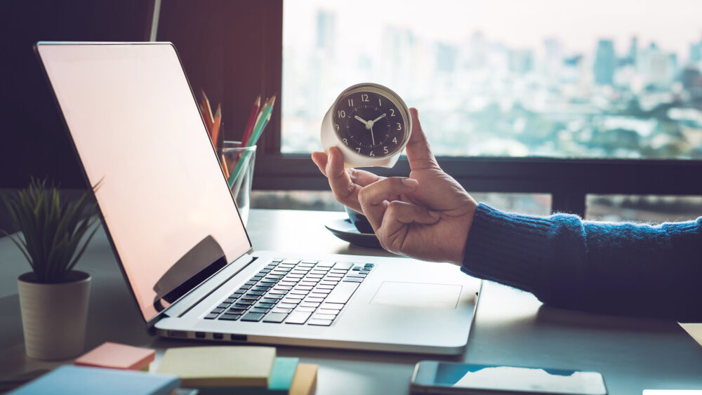 Businessman holding clock on computer laptop