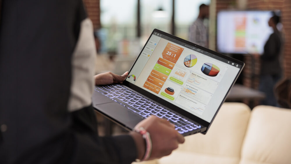 Employee holding laptop with business diagrams in company office
