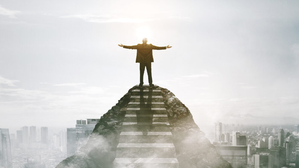 Happy successful businessman standing on mountain top after climbing stairs